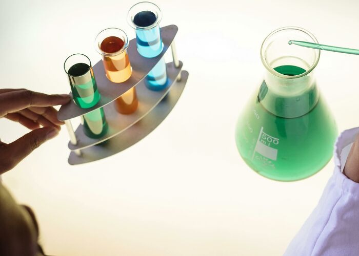 Person holding test tubes with colorful liquids next to a flask of green chemical in a lab setting sharing potentially dangerous situations