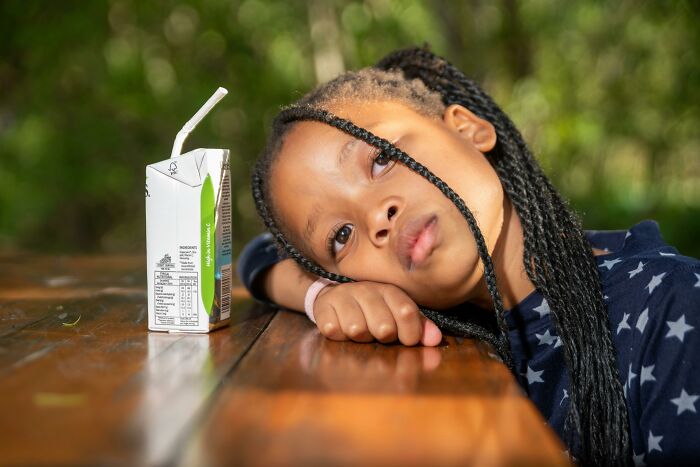 Young girl resting head on wooden table next to a drink box, illustrating frustrating genius life hacks that cause extra work