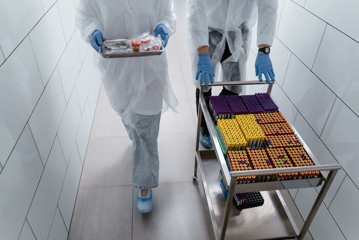 Medical staff in protective gear moving a cart of blood sample tubes, evoking scary ghost stories hospital work vibes.