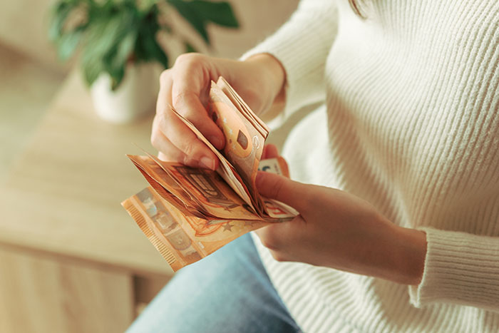 Person counting euro banknotes, illustrating a scam investment leading to zero savings and immense debt.