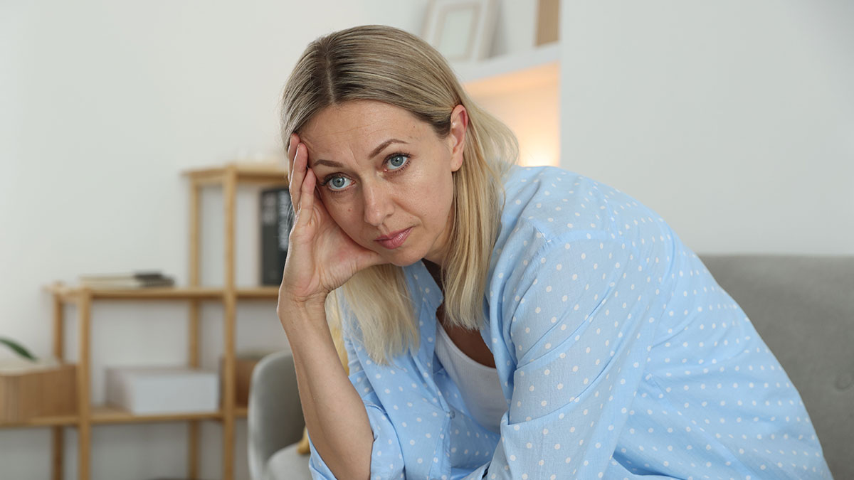 Woman looking distressed and worried at home, representing educated person falling for scam investment and debt consequences.