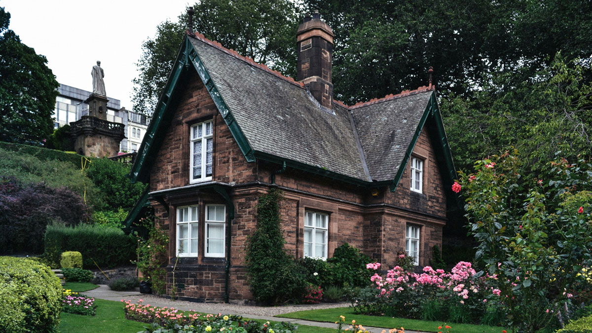 Couple standing by a tall hedge outside their stone house, refusing to cut it down for next door Airbnb's benefit.