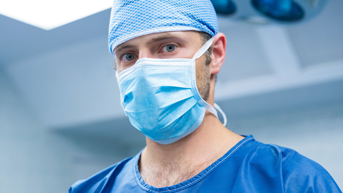 Plastic surgeon wearing surgical scrubs, mask, and cap preparing for a procedure in a medical setting.