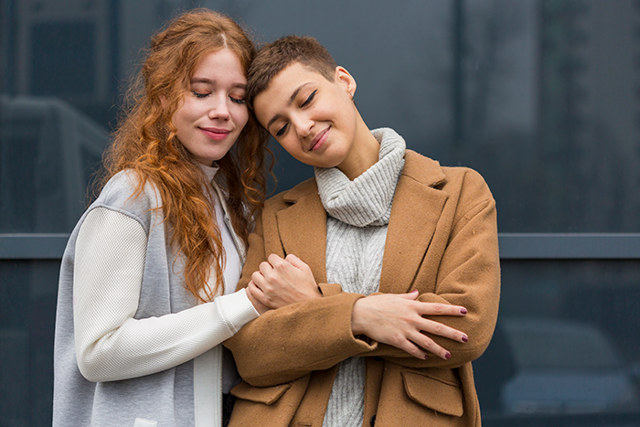Two women standing close together outdoors, showing support and comfort in a sister revealed dead brother lie situation.