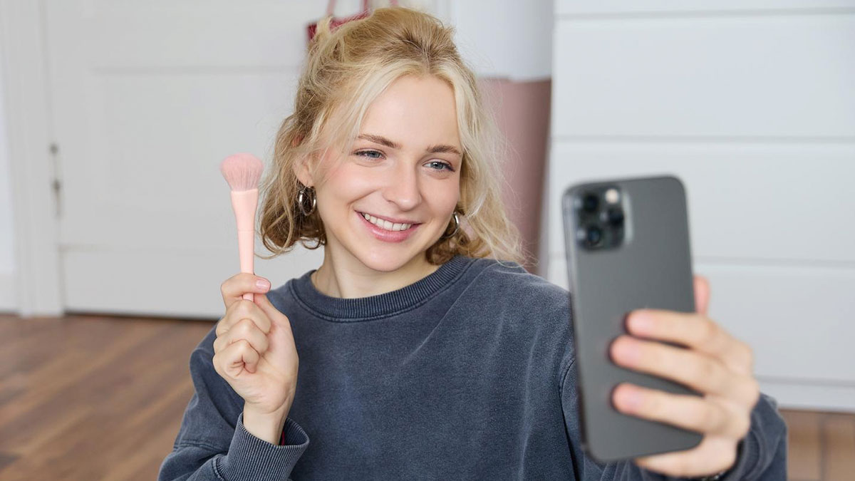 Young woman taking selfie with makeup brush, related to vegan sister and grandmau2019s leather shoes story.