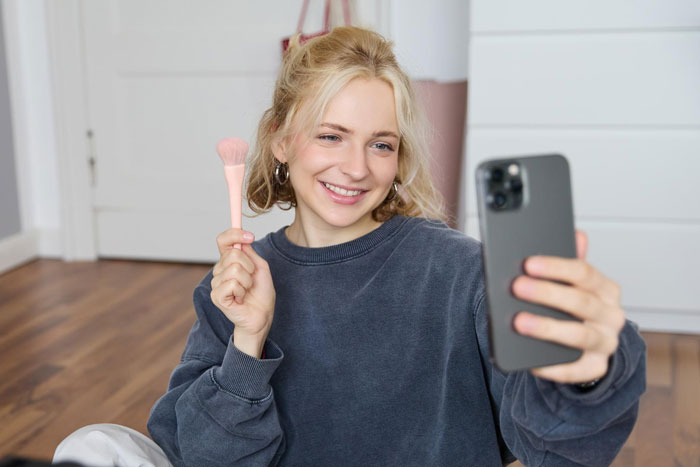 Young woman smiling while taking a selfie with a makeup brush, relating to vegan sister and leather shoes story. Young woman smiling while taking a selfie with a makeup brush, relating to vegan sister and leather shoes story.
