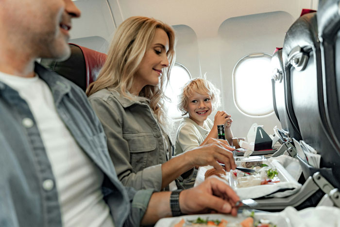 Family eating airplane meal while child looks at woman refusing to swap plane seat with rude family member Family eating airplane meal while child looks at woman refusing to swap plane seat with rude family member