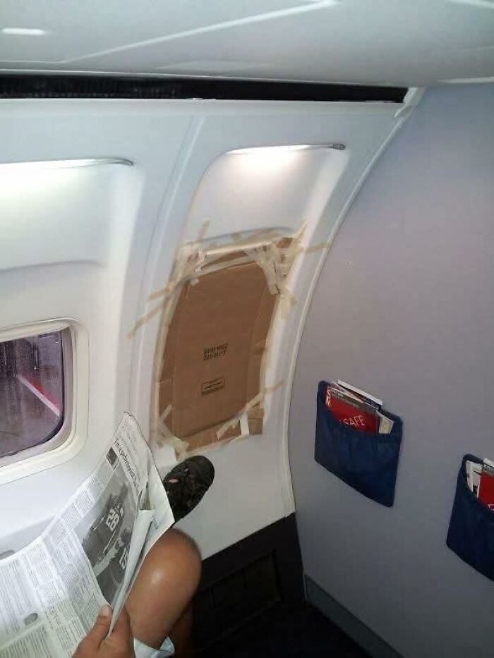 Passenger inside an airplane with a window covered by taped cardboard, highlighting absurd pleasures of the occult humor.