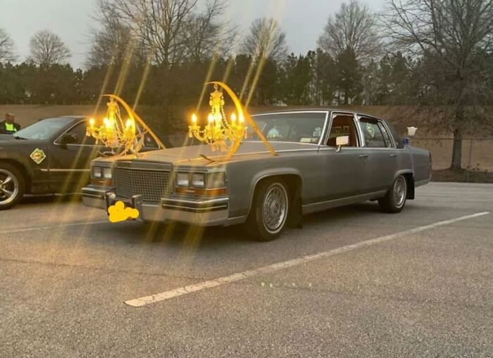Vintage car with illuminated chandeliers mounted on the hood, creating a surreal and humorous pleasures of the occult scene.