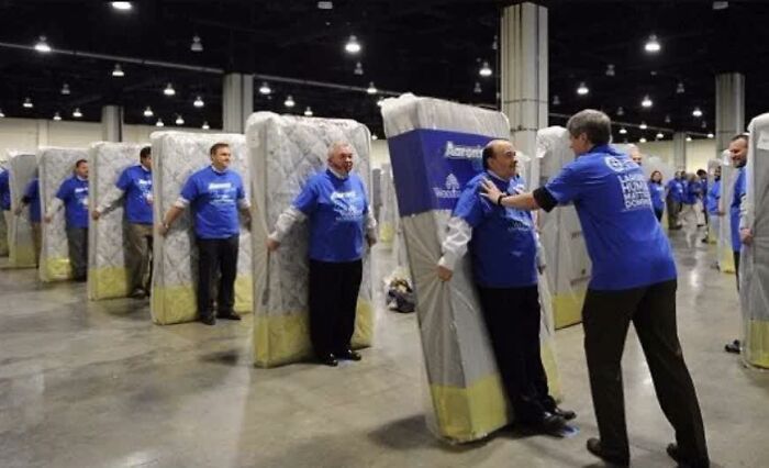 Group of people humorously posing as mattresses in a large hall, showcasing pleasures of the occult in an unexpected way.