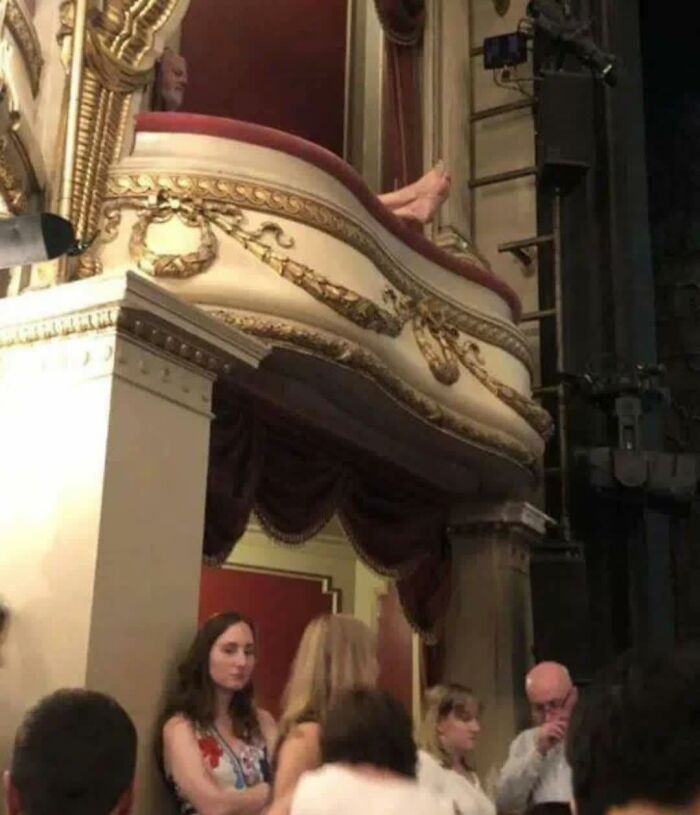 Man's feet humorously sticking out from an ornate theater balcony, creating an awkward and out of context occult scene.