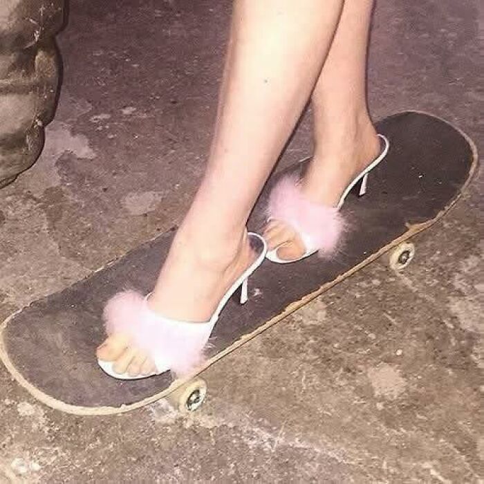 Feet wearing pink fluffy high heels standing on a skateboard, creating a humorous out of context pleasures of the occult moment.