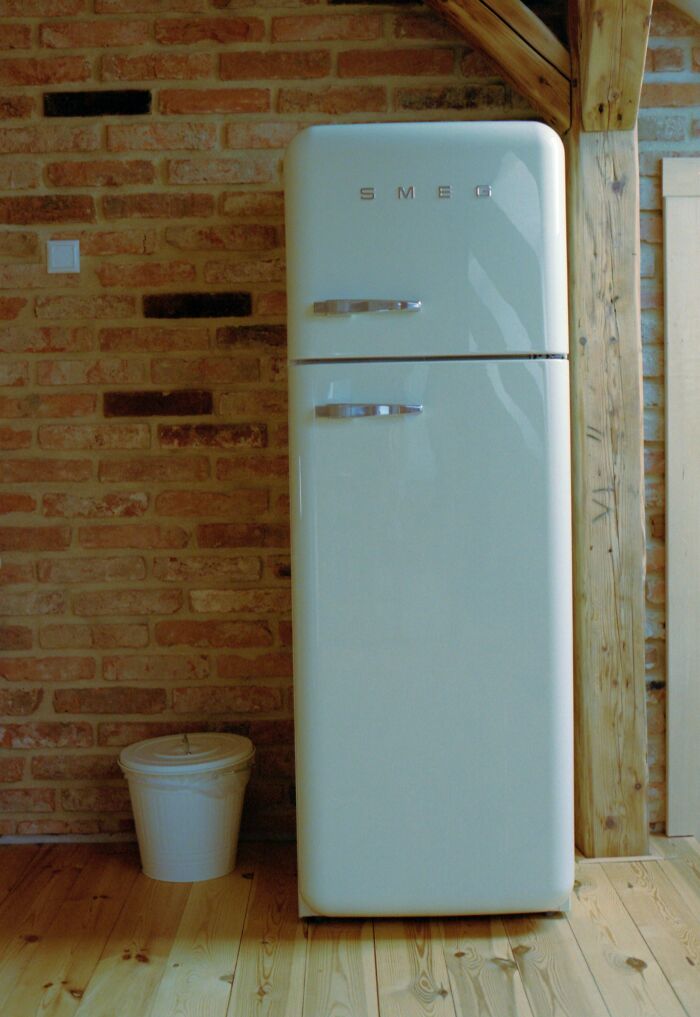 Vintage SMEG refrigerator in a rustic home interior with brick wall and wooden beams, seen by workers in strangers’ homes.