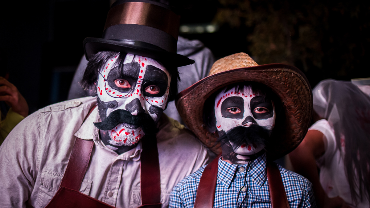 Two people with painted Halloween Dad Joke faces wearing hats and costumes at a Halloween event at night