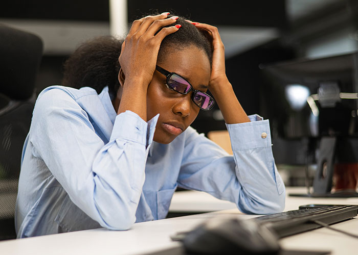 Stressed employee in glasses holding head at desk, reflecting on exposing management and HR to coworkers. Stressed employee in glasses holding head at desk, reflecting on exposing management and HR to coworkers.
