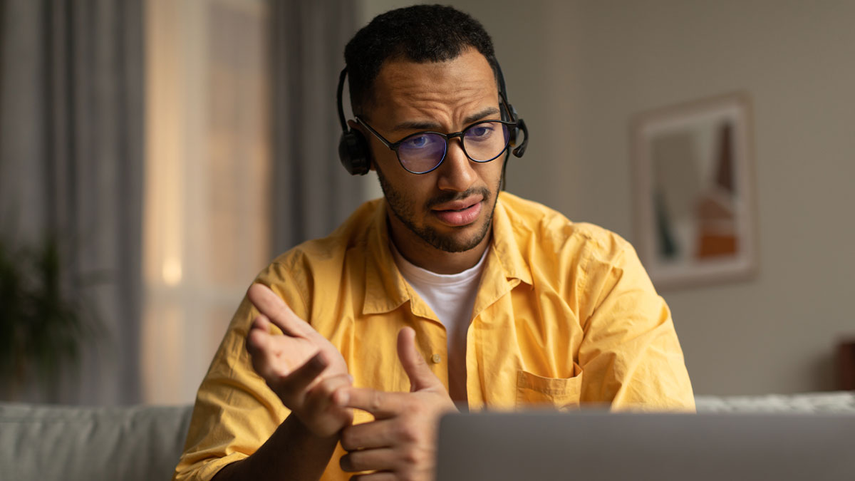 Employee wearing headset and glasses, looking confused and concerned during an online work call at home.