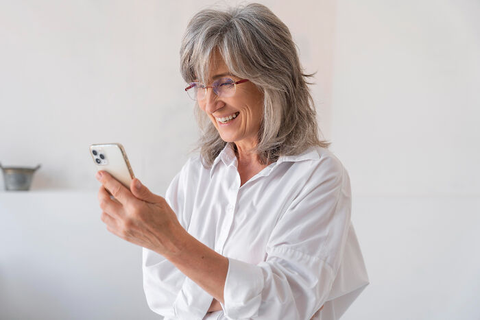 51-year-old woman smiling while looking at her phone, feeling insecure about boyfriend and his ex&rsquo;s attention