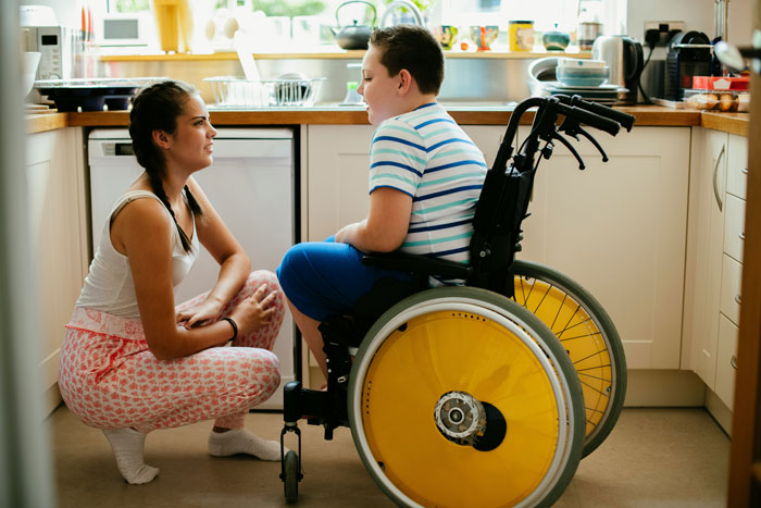 Babysitter talking to disabled child in wheelchair at home, showing concern while caring for special needs kid. Babysitter talking to disabled child in wheelchair at home, showing concern while caring for special needs kid.