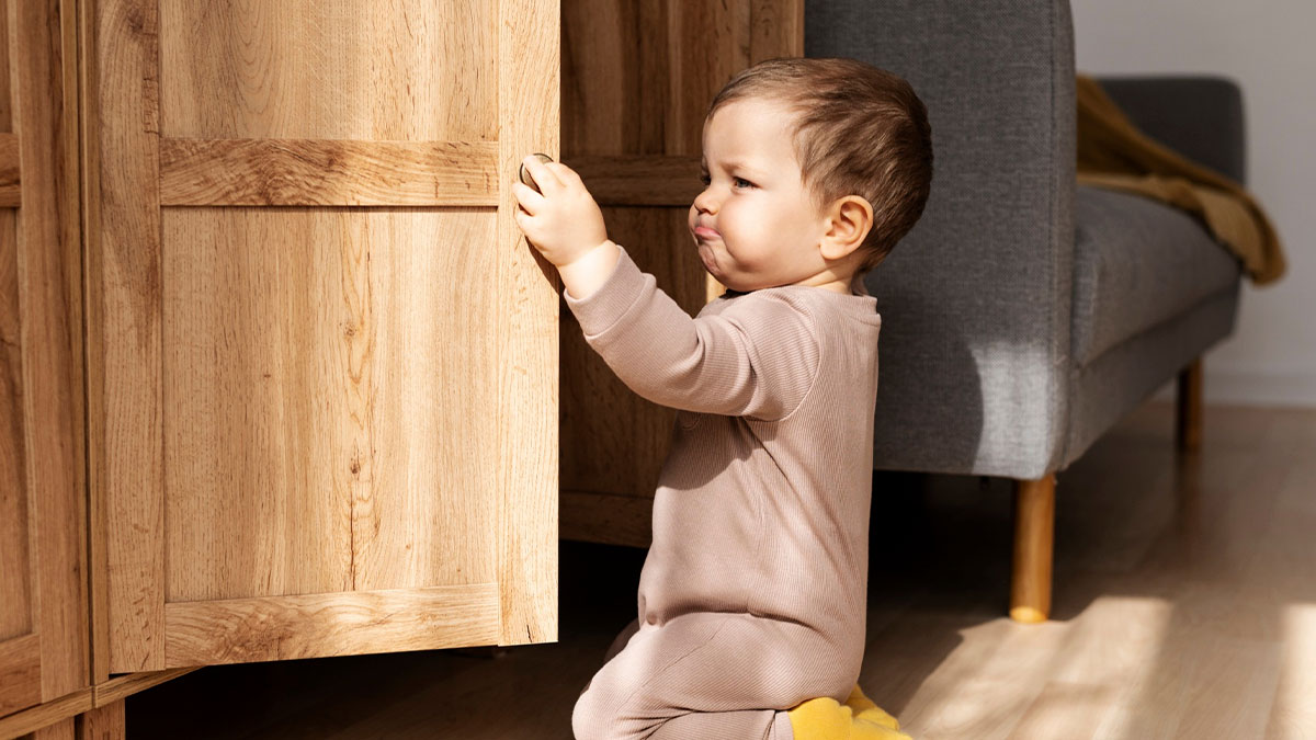 Baby nephew refusing childproofing while reaching for cabinet door in new house with natural light and modern furniture.