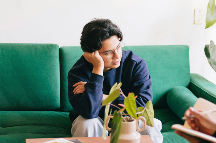 Young man looking pensive on a green sofa, portraying emotions related to refuse living with disabled sibling challenges. Young man looking pensive on a green sofa, portraying emotions related to refuse living with disabled sibling challenges.