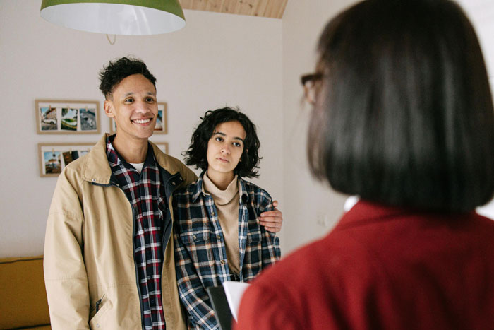 A young couple standing together, discussing family dynamics with a woman in an office setting about bio mom and stepmom.