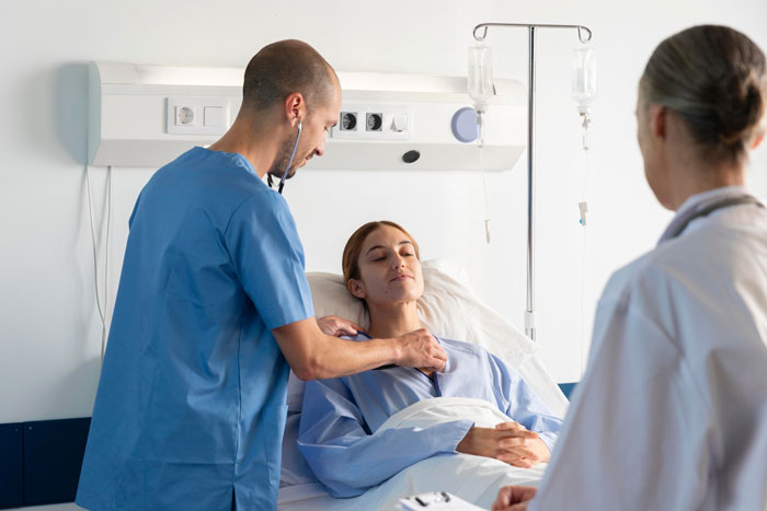 Man in scrubs using stethoscope to check woman patient resting in hospital bed, illustrating refuse visiting girlfriend hospital concept.