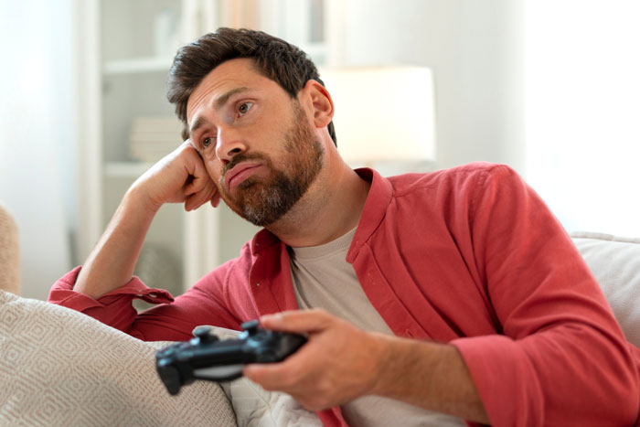 Manchild playing video games, looking bored and distracted while holding a game controller on a couch. Manchild playing video games, looking bored and distracted while holding a game controller on a couch.