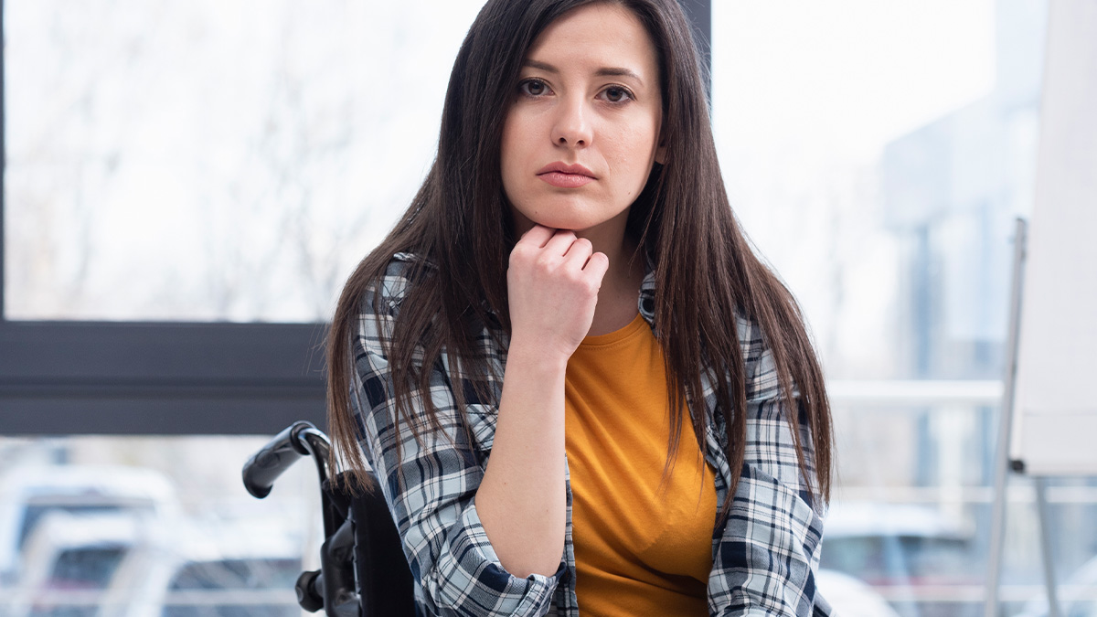 Young paralyzed woman in wheelchair looking serious wearing casual clothes indoors at home or office environment