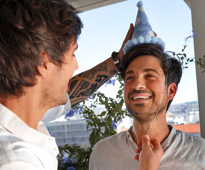 Two men celebrating a birthday with a party hat, highlighting surprise and friendship during a birthday trip event.