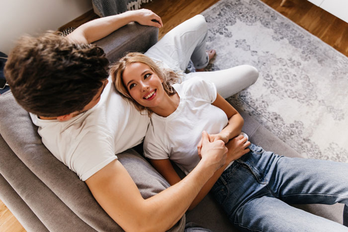 Young couple relaxing together on a couch, smiling and holding hands, illustrating relationship break every year concept. Young couple relaxing together on a couch, smiling and holding hands, illustrating relationship break every year concept.