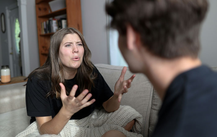 Woman expressing frustration during a serious relationship break conversation with a man on a couch at home.