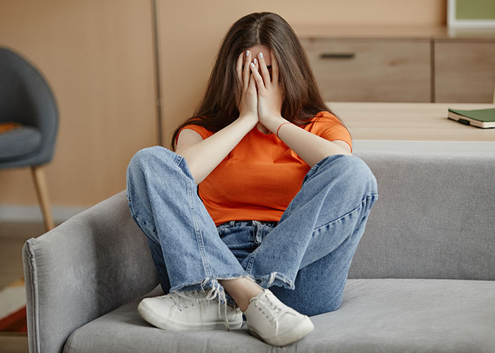 Young woman in orange shirt sitting on couch upset over rich boyfriend demands equal split rent refused Young woman in orange shirt sitting on couch upset over rich boyfriend demands equal split rent refused