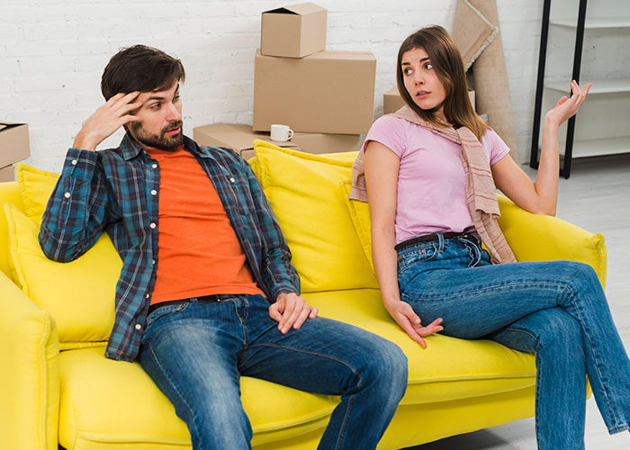 Young rich boyfriend and girlfriend sitting on yellow couch arguing about equal split rent during move. Young rich boyfriend and girlfriend sitting on yellow couch arguing about equal split rent during move.