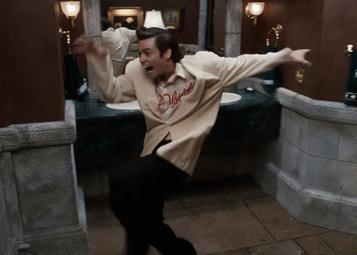 Man in a beige shirt reacting dramatically in a restroom, illustrating ridiculous reasons that ended up in the emergency room.