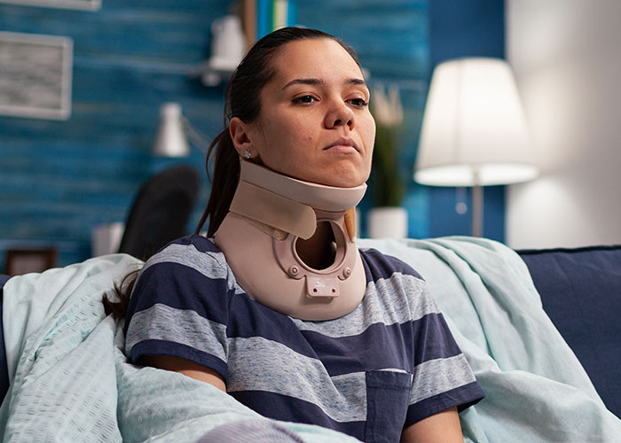 Woman wearing neck brace sitting on couch recovering from ridiculous reasons that ended up in the emergency room.