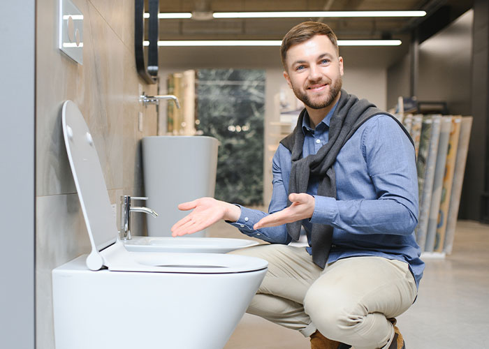 Man in casual clothes pointing at a toilet in a showroom, illustrating ridiculous reasons ended up emergency room.