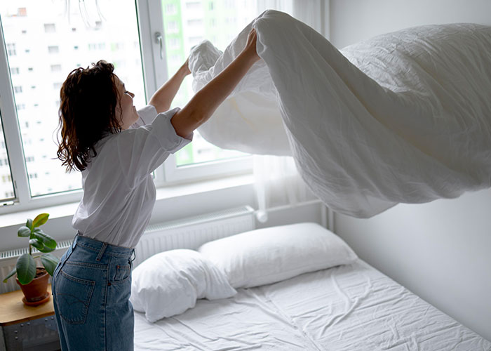 Woman making bed in a bright room, illustrating one of the ridiculous reasons people ended up in the emergency room.