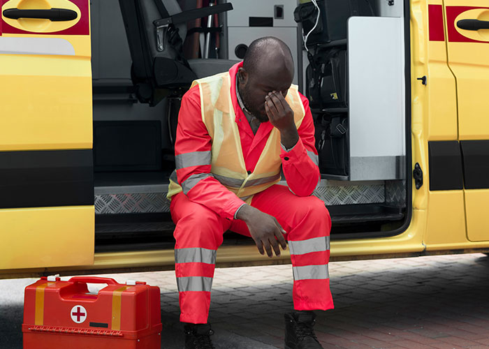 Paramedic sitting exhausted by ambulance door, medical kit nearby, highlighting ridiculous reasons ended up emergency room.