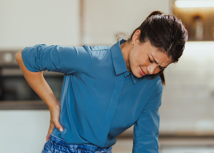 Young woman in blue shirt holding her back in pain, illustrating ridiculous reasons that ended up in the emergency room.
