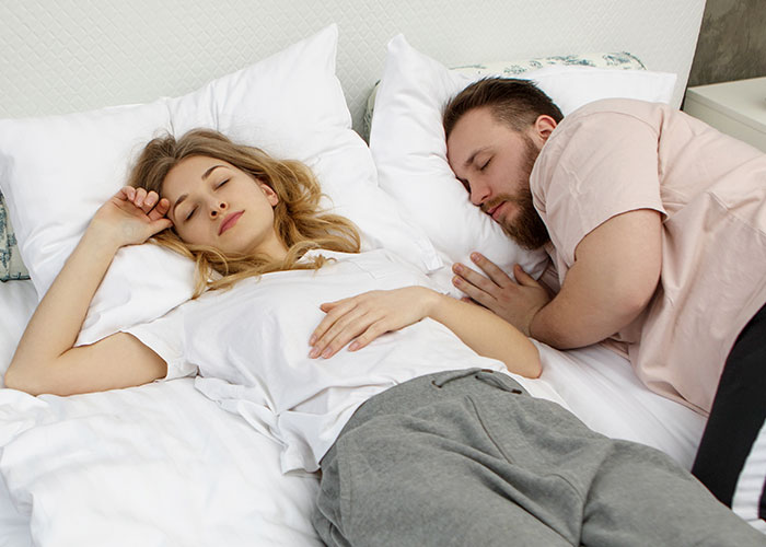 Young man and woman lying on bed asleep, illustrating ridiculous reasons that ended up in the emergency room situation.