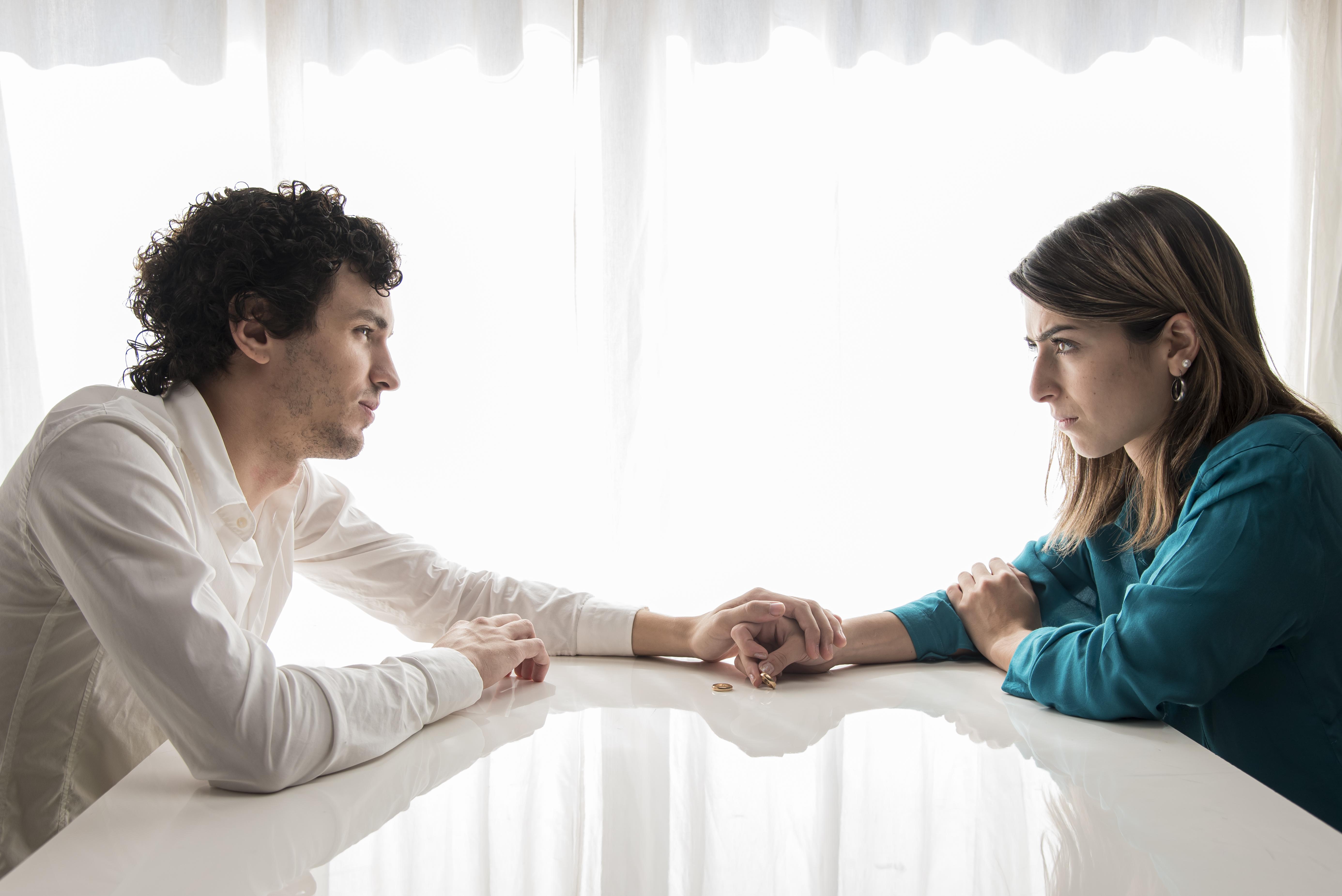 Woman demanding combined income while arguing with boyfriend in a tense moment at a white table with wedding rings. Woman demanding combined income while arguing with boyfriend in a tense moment at a white table with wedding rings.