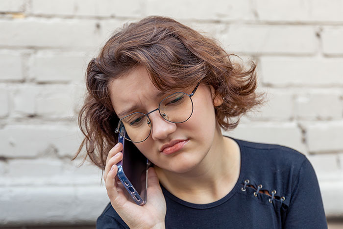 Teen with glasses looking upset while talking on phone, reflecting anger and sadness about being dumped at boarding school. Teen with glasses looking upset while talking on phone, reflecting anger and sadness about being dumped at boarding school.