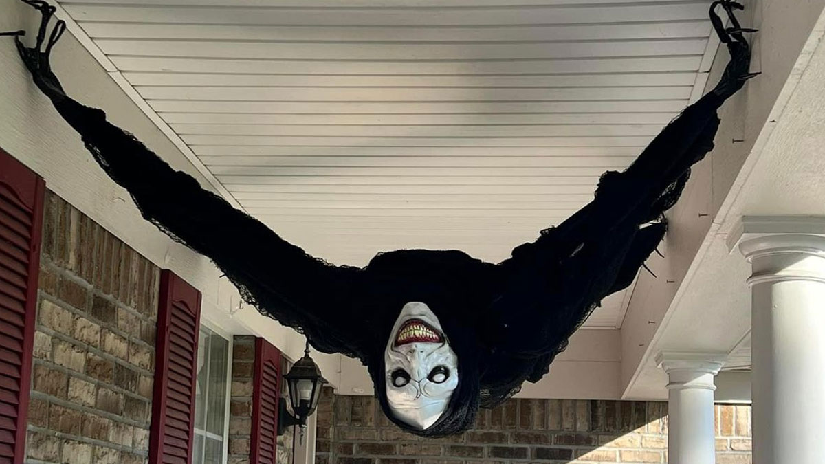 Scary outdoor Halloween decoration hanging upside down on a porch with white columns and brick walls.