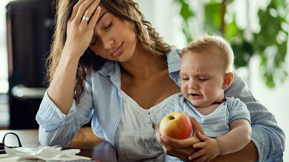 Tired mother holding baby looking frustrated as she deals with challenges of absentee husband and family concerns.
