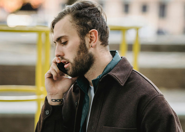 Young man in a coat talking seriously on phone, reporting sister to CPS about her illegal adoption plan.