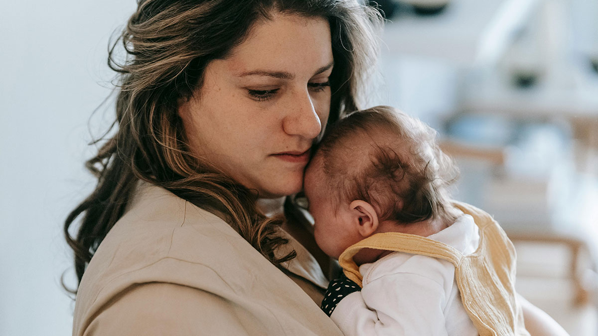 Woman holding a baby closely indoors, representing themes of illegal adoption and child protective services involvement.