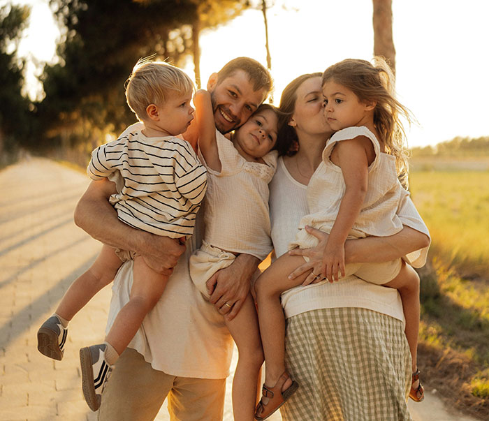 Mom of 4 holding her children outdoors during sunset, illustrating challenges with group activities and social dynamics. Mom of 4 holding her children outdoors during sunset, illustrating challenges with group activities and social dynamics.