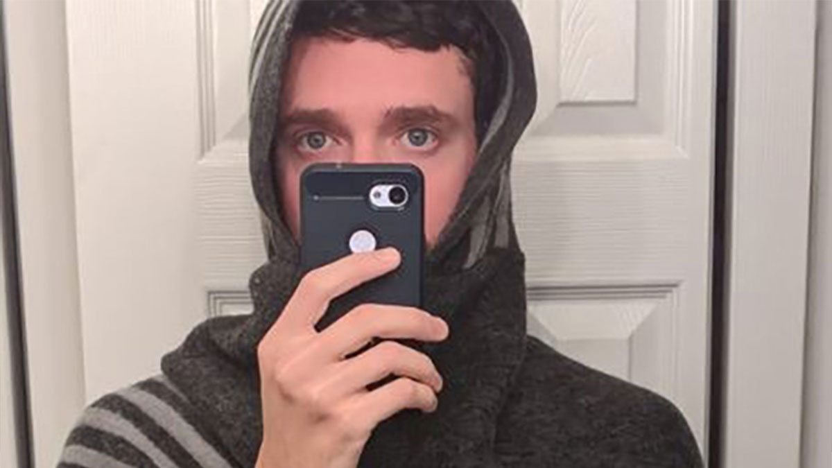 Man wearing a dark shawl and taking a mirror selfie with smartphone, highlighting guys buying shawls trend.