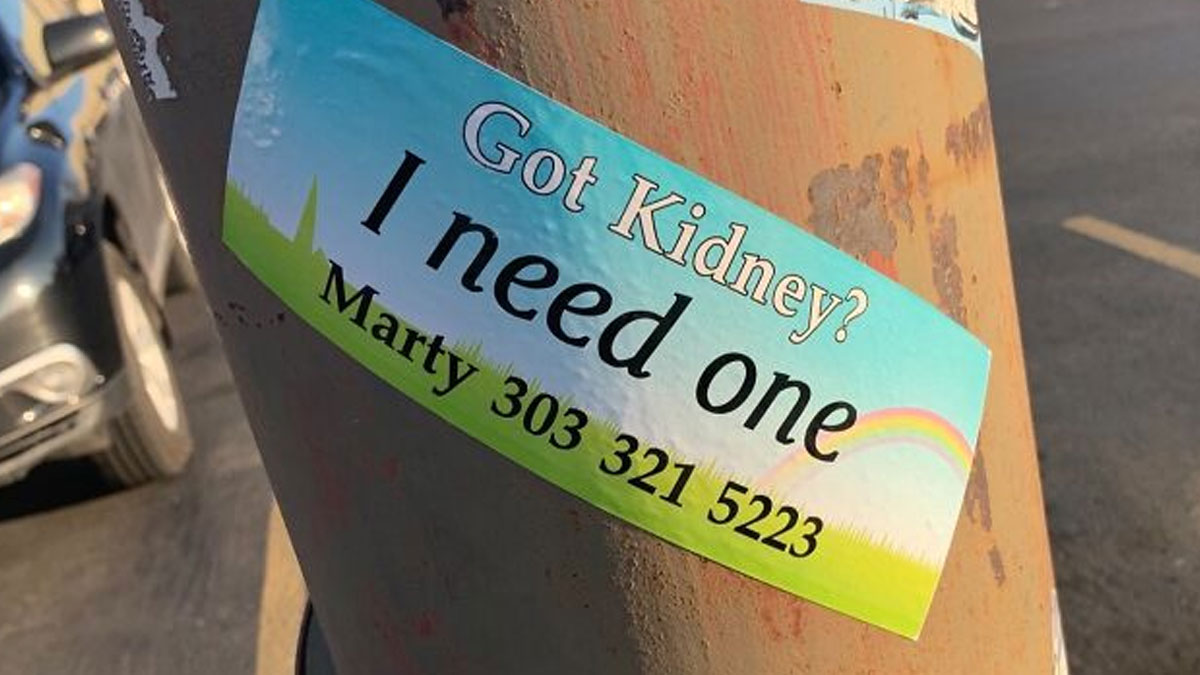 Sticker on a rusty pole showing a kidney donation plea with contact info, highlighting harsh realities of American healthcare.