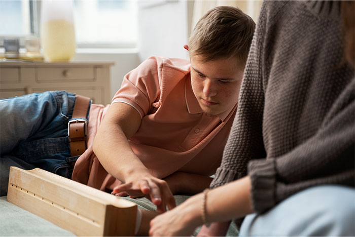 Teen autistic boy playing a wooden game with a woman, highlighting care and challenges in autism family support.